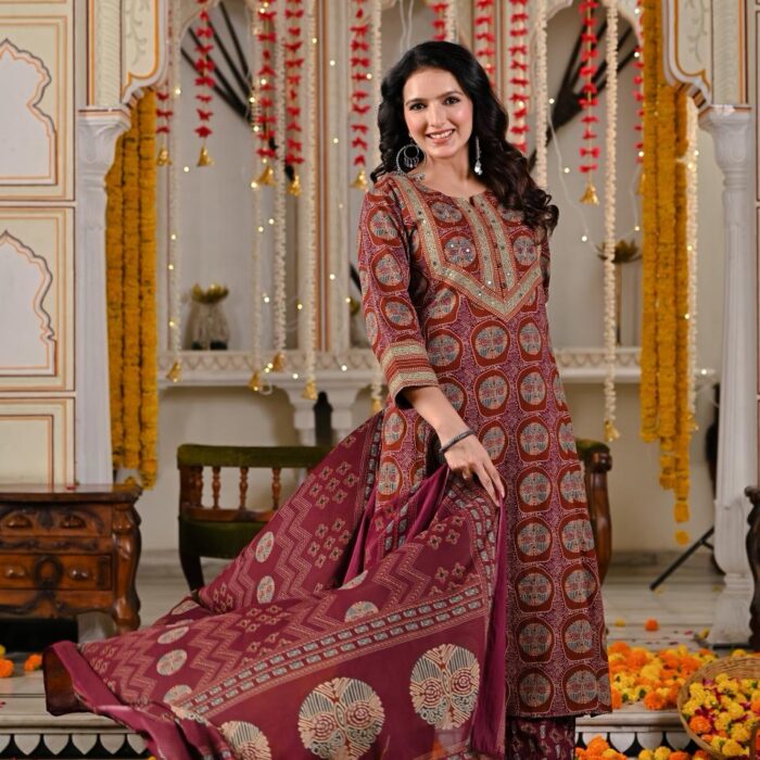 Woman wearing a premium maroon printed cotton kurta with matching pants and a flowy dupatta, standing in a traditional Rajasthani décor setting by HK Vastra.
